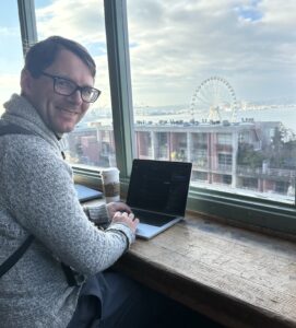Tom working on laptop on a counter in front of large windows.